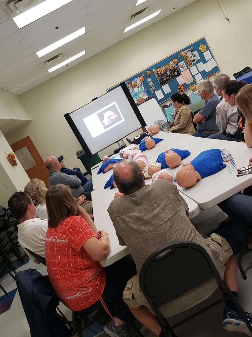 People gathered around a table watching a presentation on a projector screen in a classroom.
