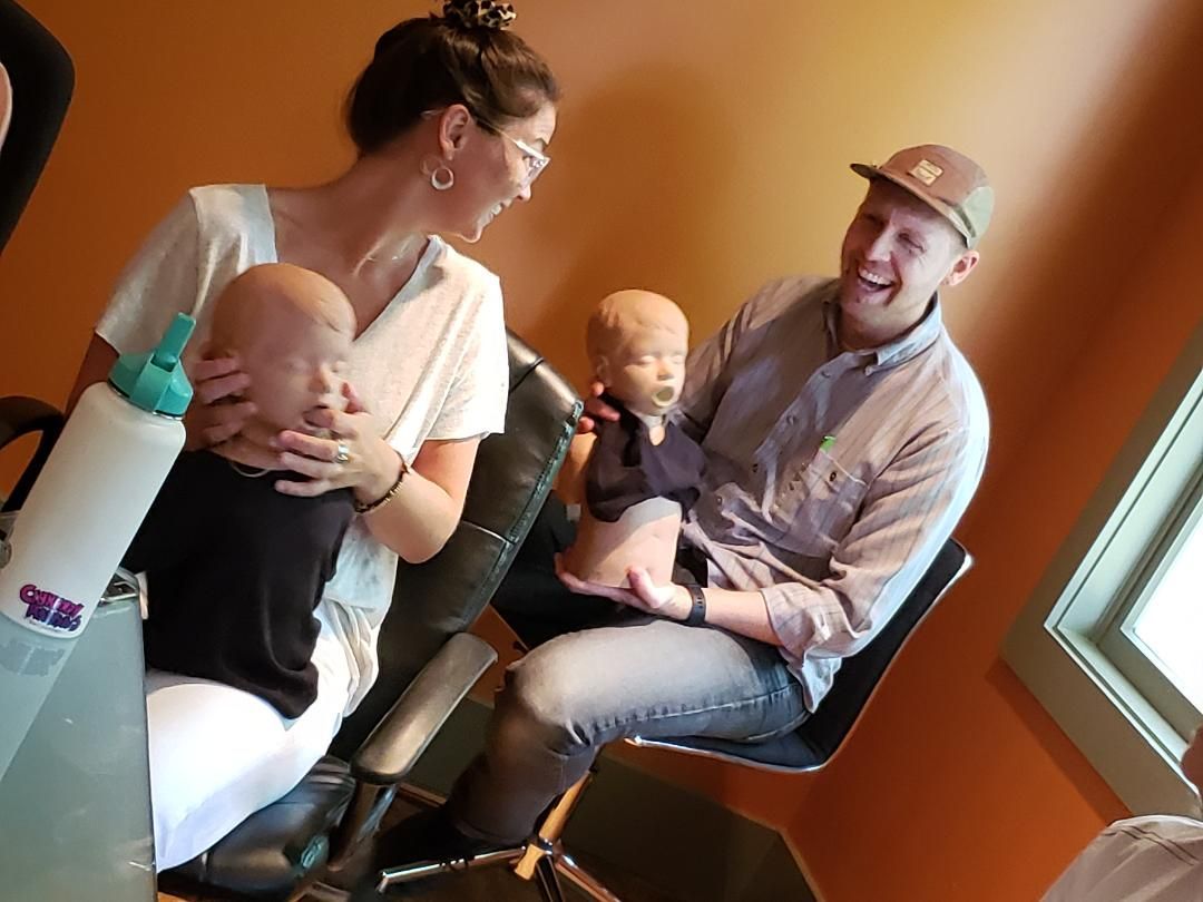 Two adults holding two babies in a cozy orange room near a window