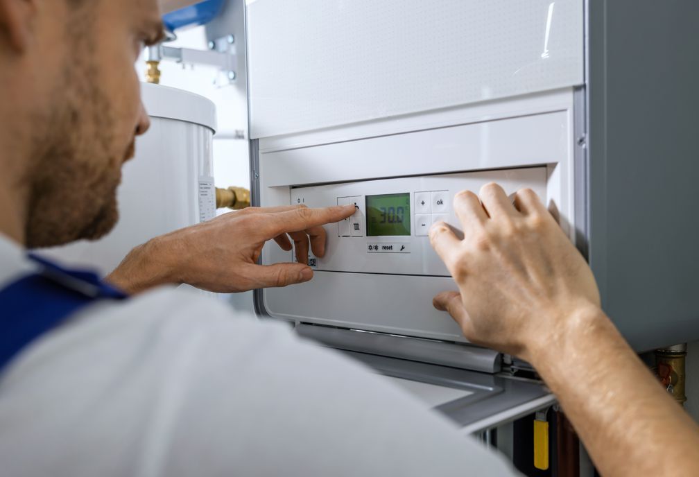 Man in blue-collared shirt adjusting controls on a white heating unit with a small screen.