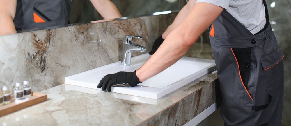A person wearing black gloves installs a bathroom sink in a bathroom.