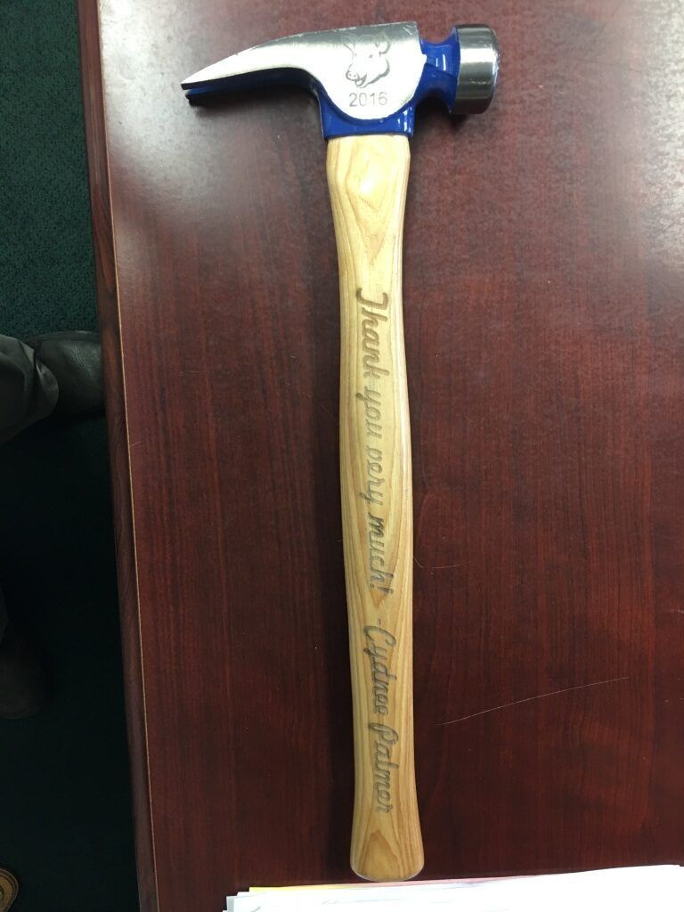 Blue-and-silver claw hammer with a wooden handle on a dark wood surface
