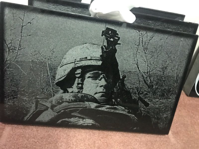 Black-and-white framed photo of a soldier in a helmet, with a raised rifle against a bare tree background.