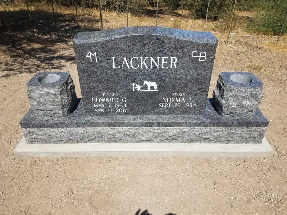 Black granite cemetery headstone engraved “Lackner,” with two small flower holders on a gravel base.