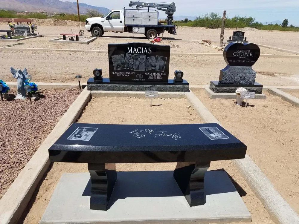 Black memorial bench and gravestones in a desert cemetery, with a white truck in the background.