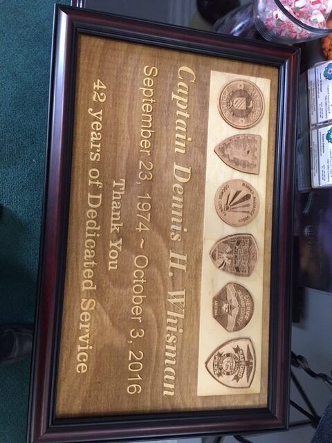 Framed military retirement plaque with five service medals and engraved dedication text, on a teal surface