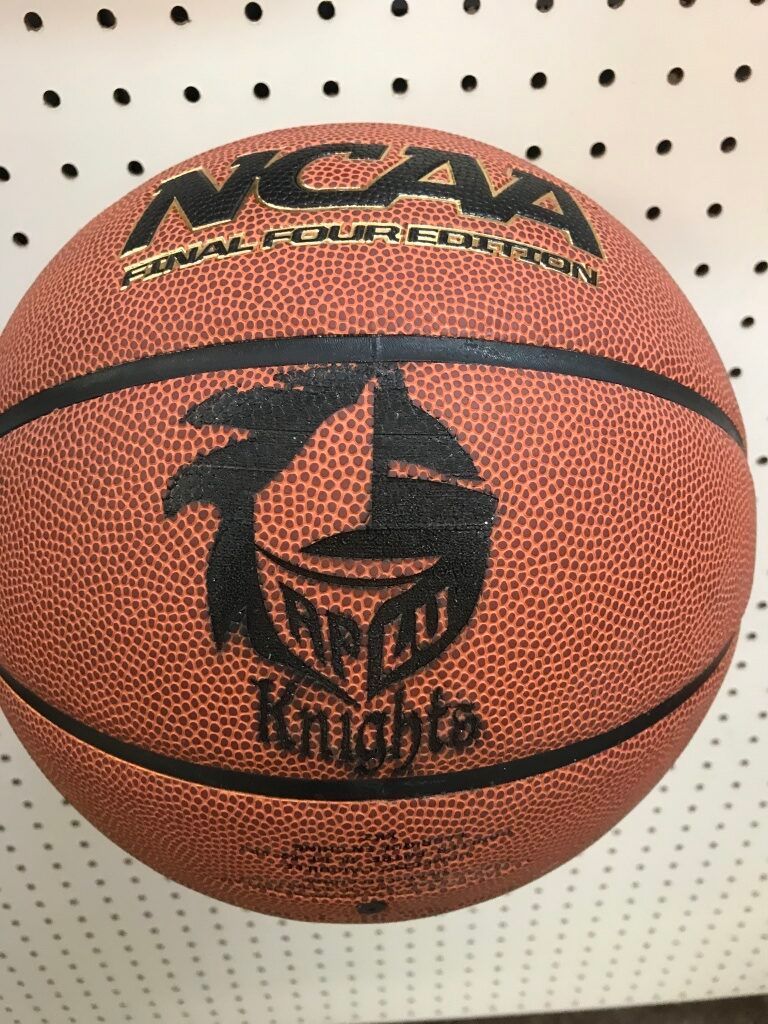 Orange NCAA basketball with black logos against a white perforated wall.