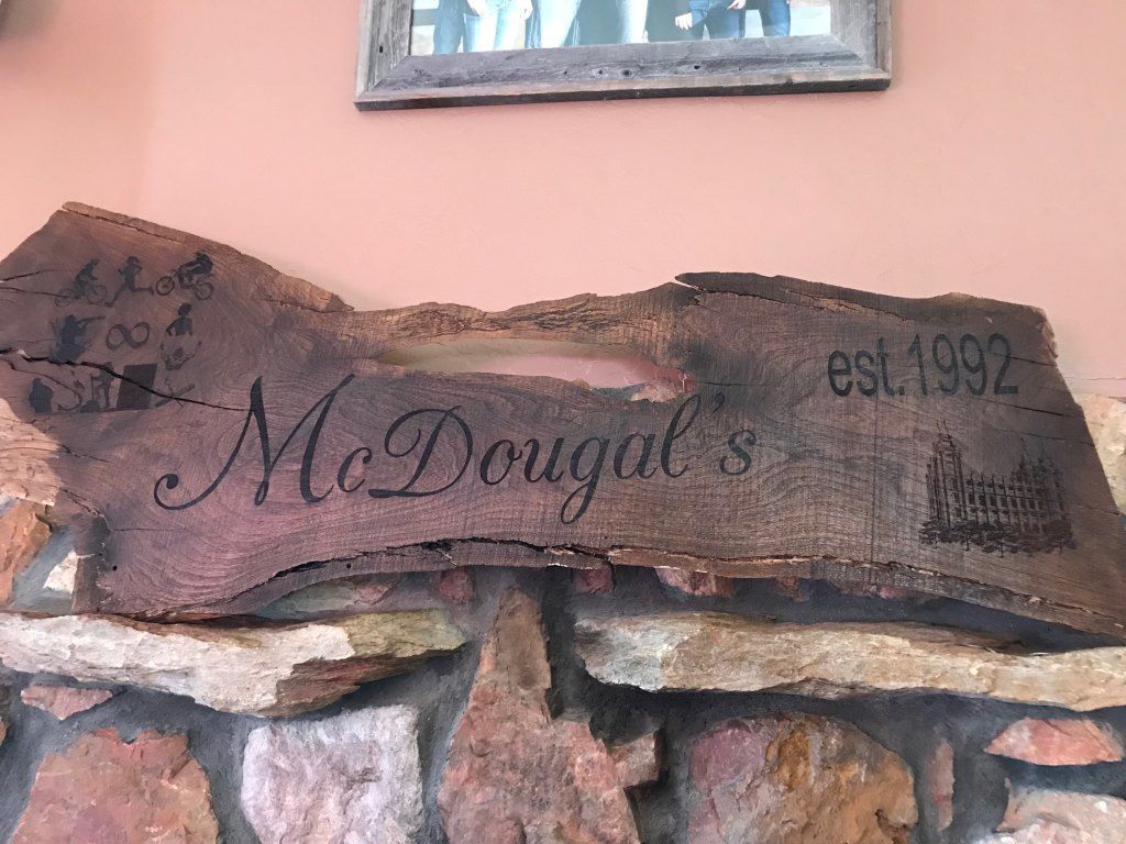Wooden sign reading “McDougals” and “est. 1992” mounted on a stone wall against a peach exterior wall