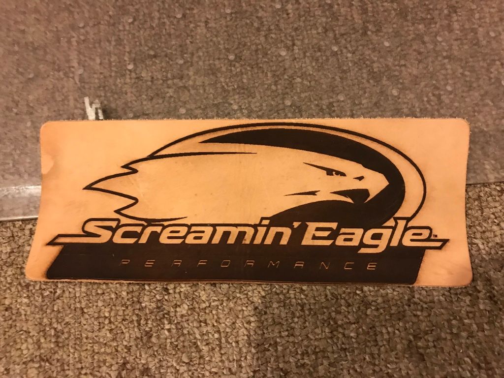 Orange Screamin’ Eagle logo sign with black eagle graphic on a carpeted floor