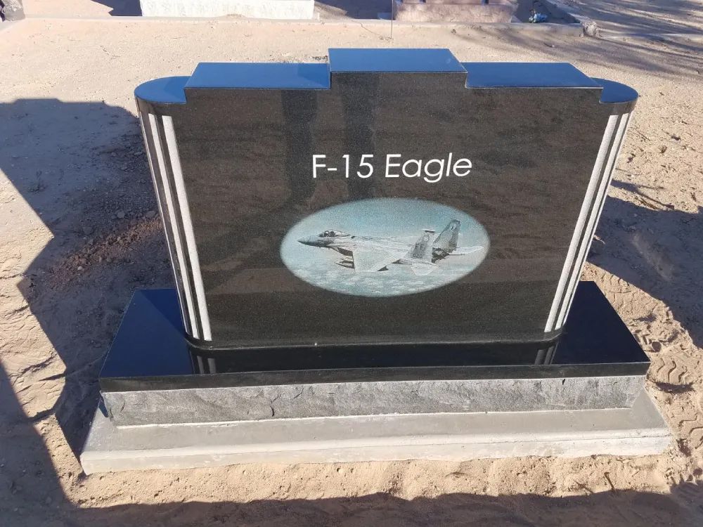 Black memorial plaque labeled “F-15 Eagle” with an aircraft image on a stone base outdoors