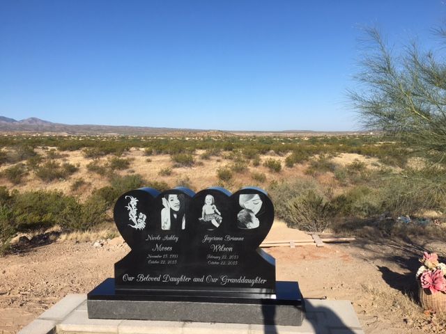 Black memorial headstone with photos in a desert cemetery under a clear blue sky