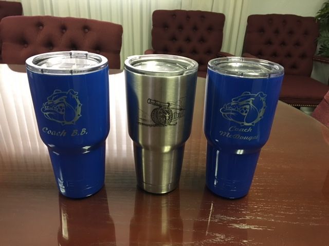 Three insulated tumblers on a wooden table, two blue and one silver, with a tufted chair in the background