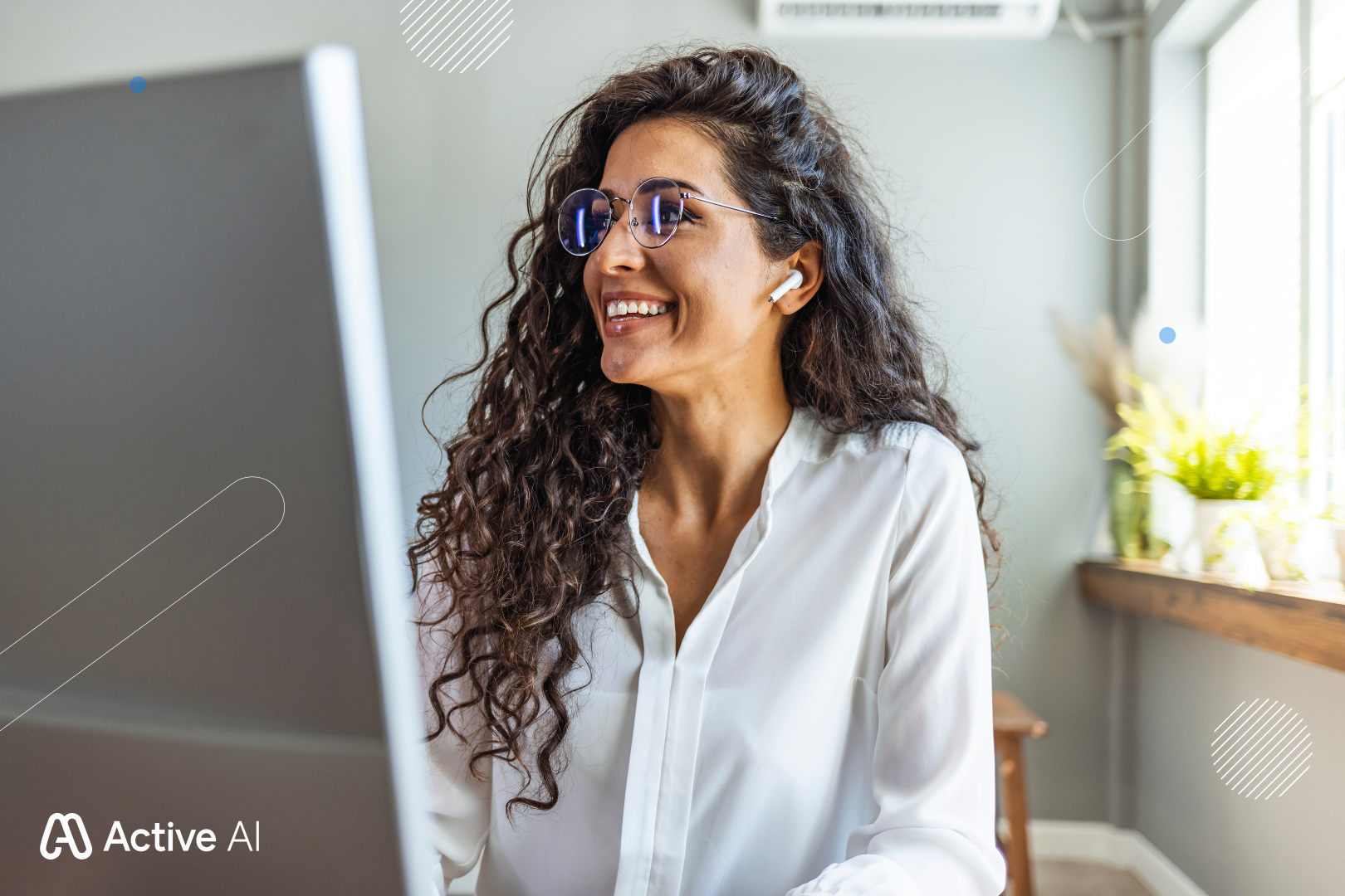 Woman wearing glasses and earbuds, smiling while working at a computer in a home office.