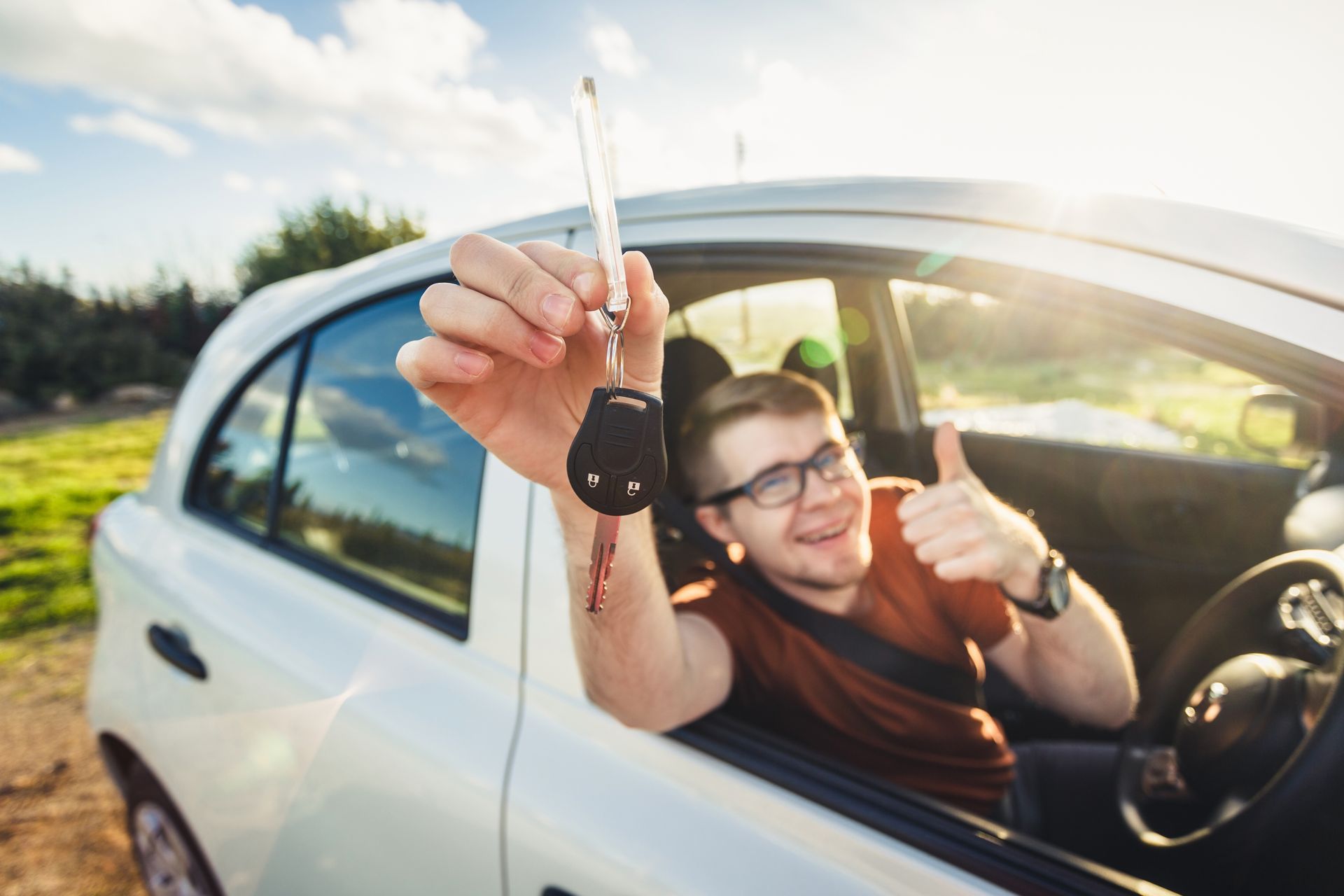 A man in a car is holding a car key and giving a thumbs up