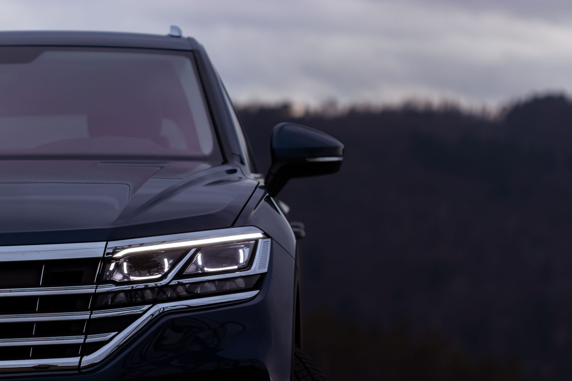 Front-left view of a black SUV with headlights on against a dark, blurred outdoor background Front-left view of a black SUV with headlights on against a dark, blurred outdoor background