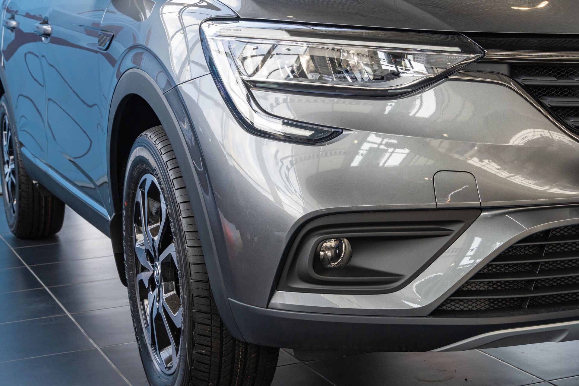 Silver SUV front corner in a showroom, showing headlight, grille, and wheel Silver SUV front corner in a showroom, showing headlight, grille, and wheel