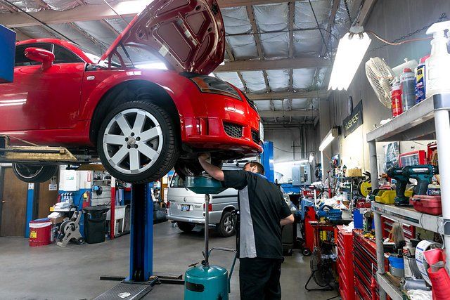 Mechanic working on a red car raised on a lift in a garage.