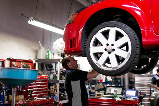 Mechanic working under a red car on a lift in a garage.