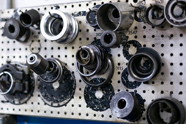 Assorted metal machine parts mounted on a pegboard in a workshop.