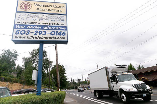 Sign for Working Class Acupuncture and Hillside Imports; truck on road.