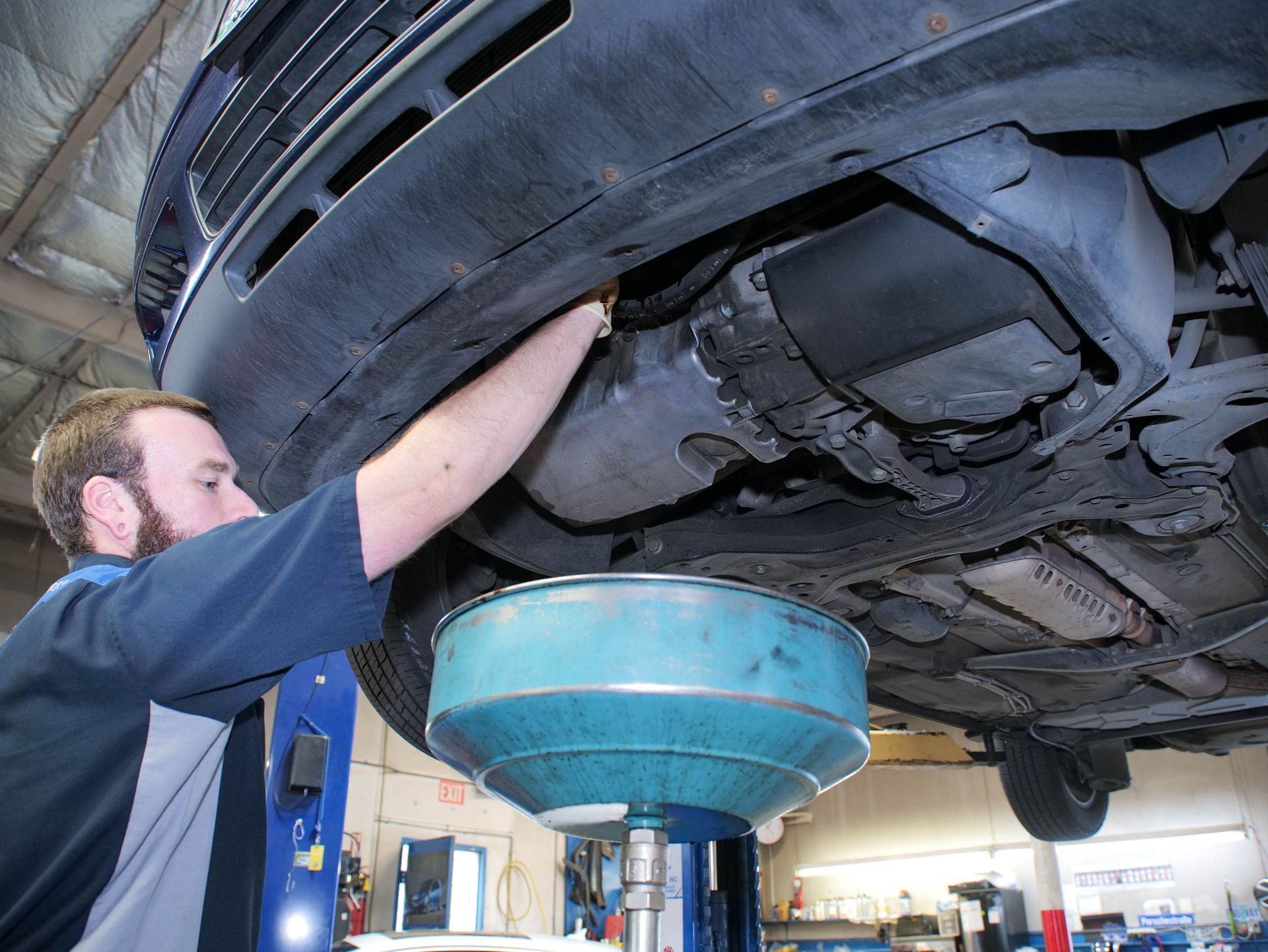 Mechanic changing oil on a car, positioned under the vehicle with a catch pan.