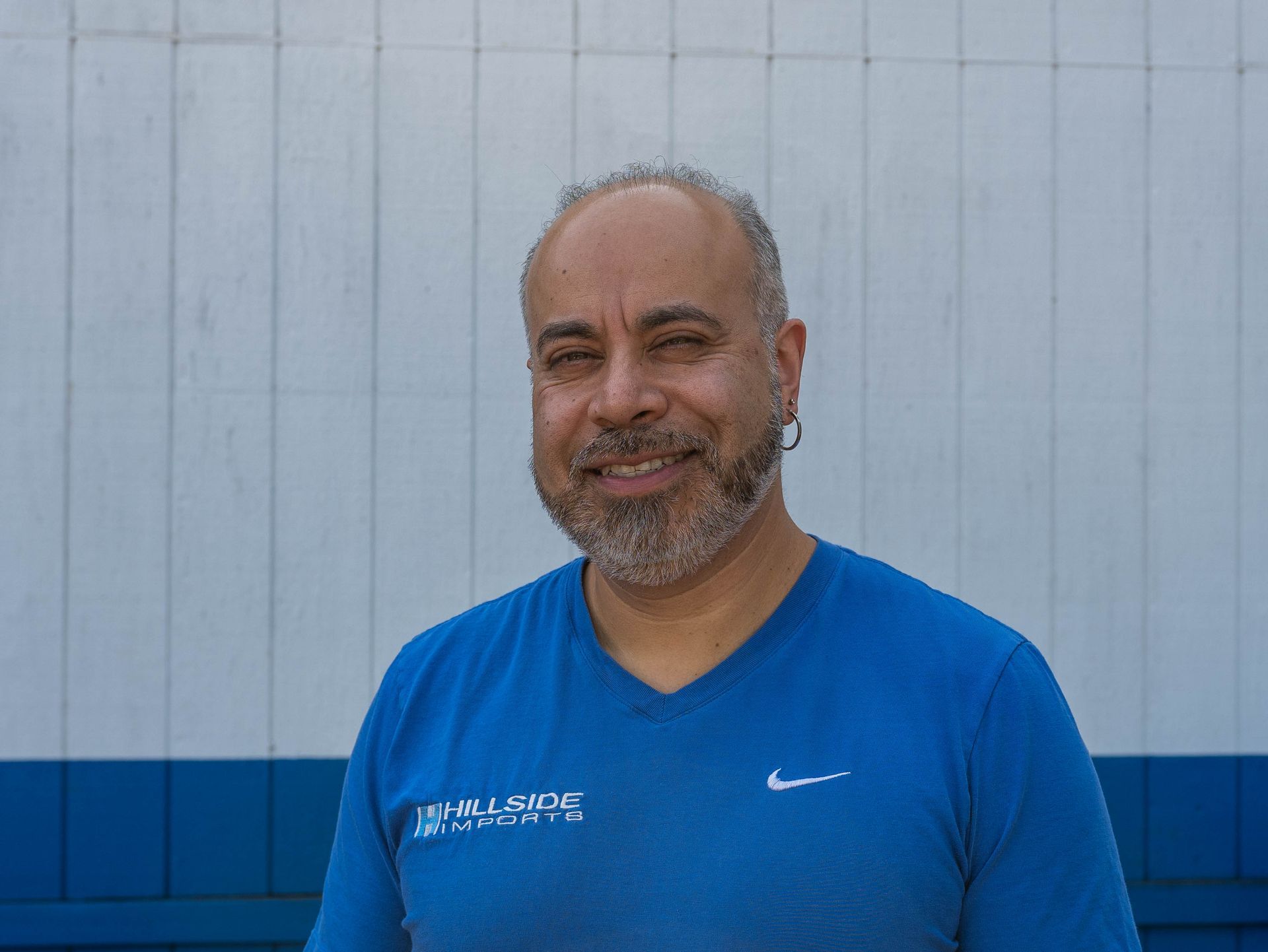 Man in blue shirt smiles, standing in front of a blue and white wall.