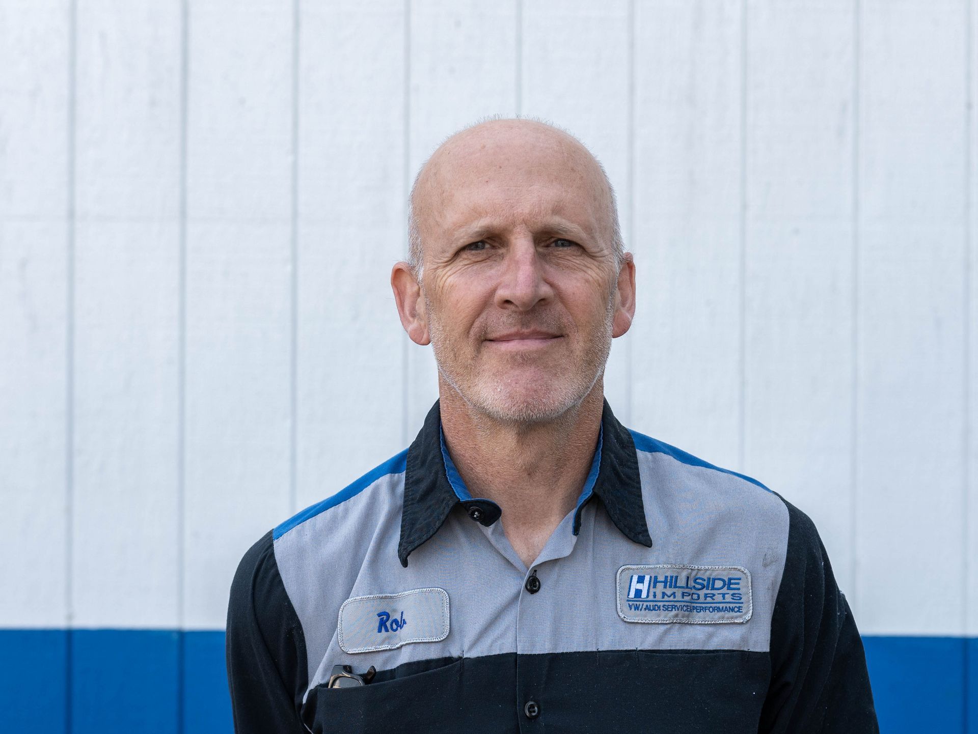 Man with bald head in mechanic's uniform stands in front of a building.