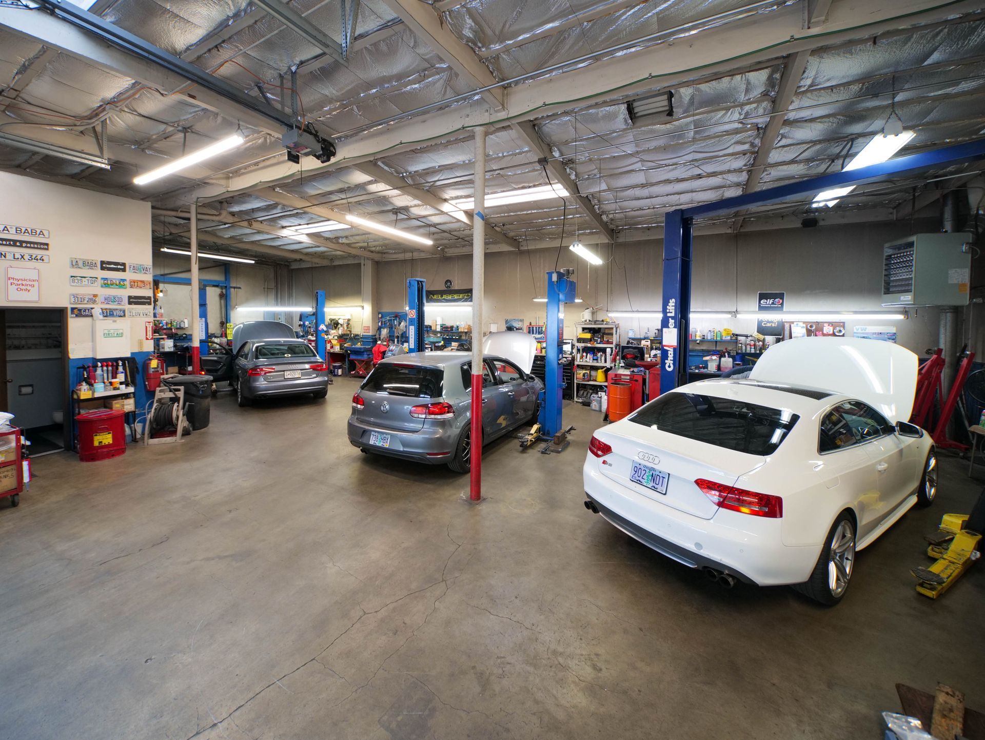 Auto repair shop with several cars on lifts. Concrete floor, overhead lights, tools and equipment visible.