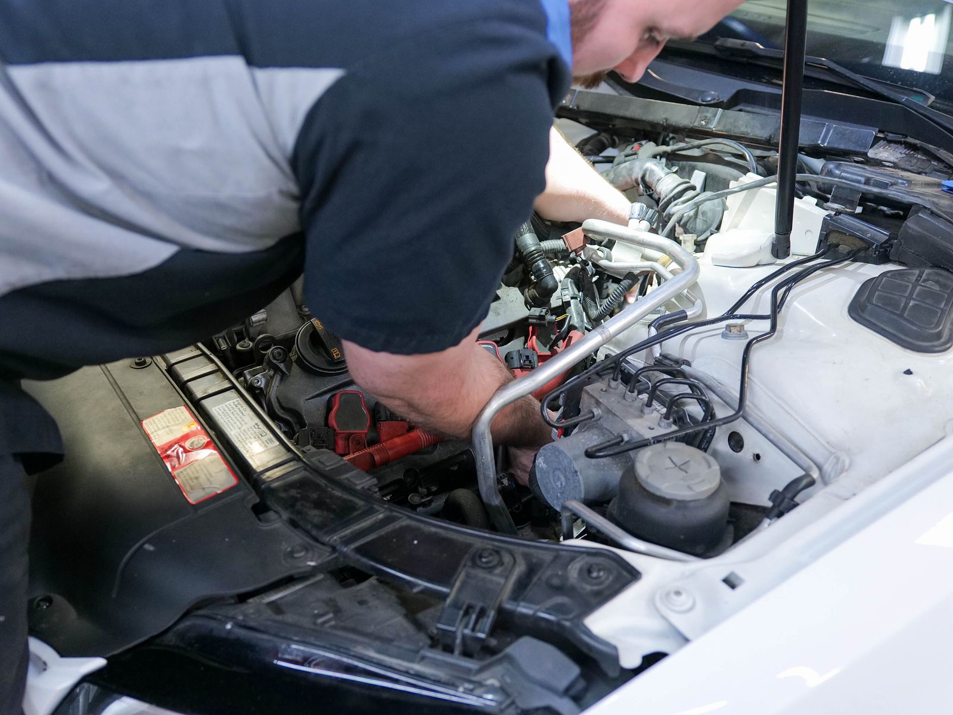 Mechanic working on a car engine under the hood. White car, hands reaching in.