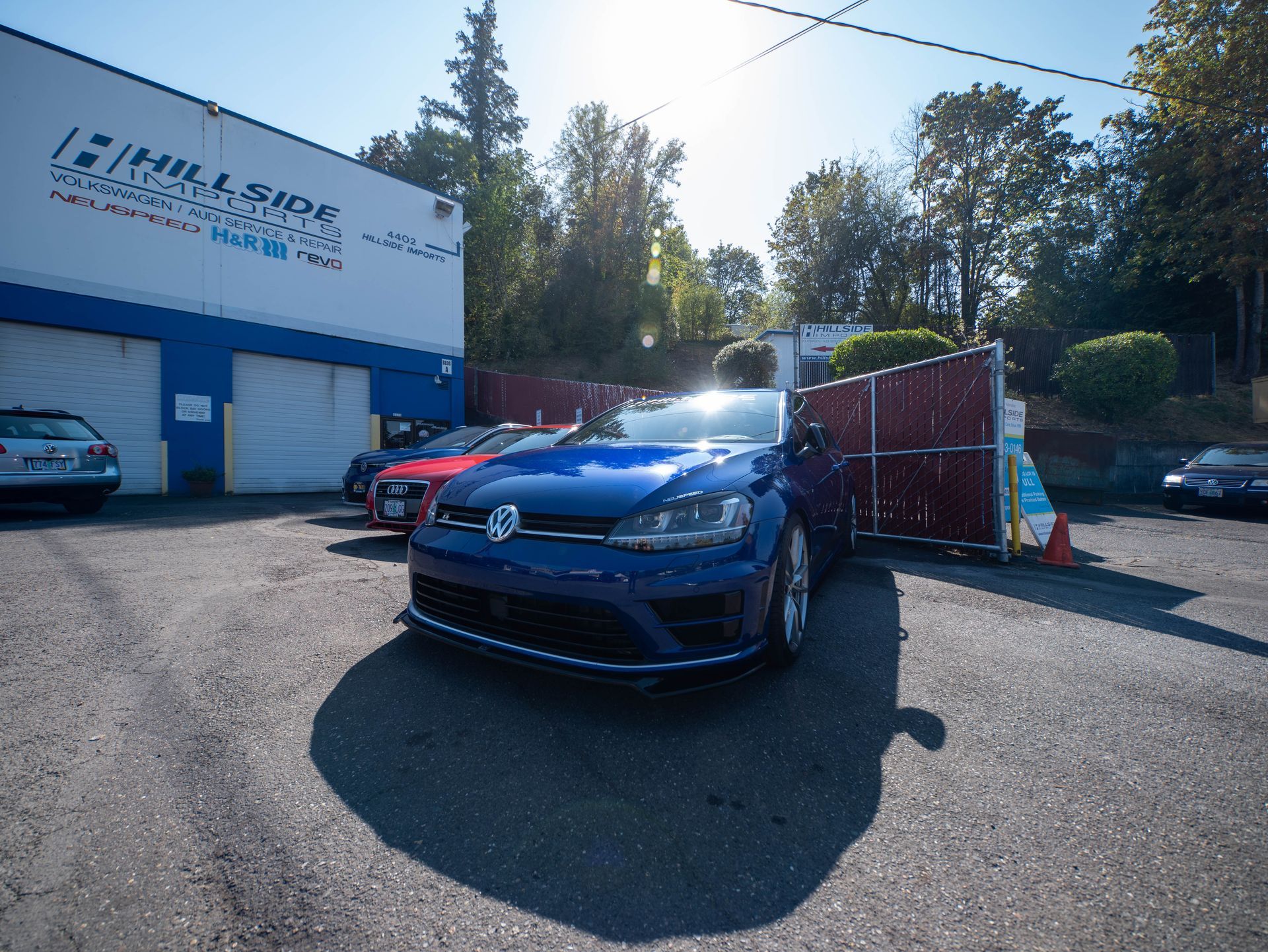Blue car parked in front of auto repair shop with blue and white building, sunny day.
