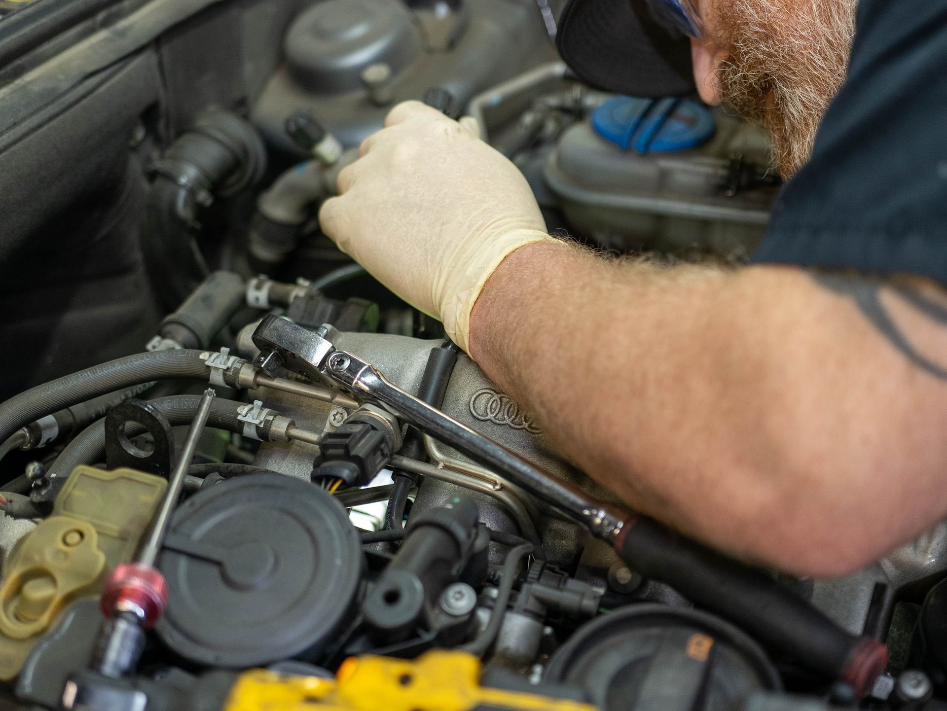 Mechanic using a wrench on a car engine, wearing gloves, in a garage.