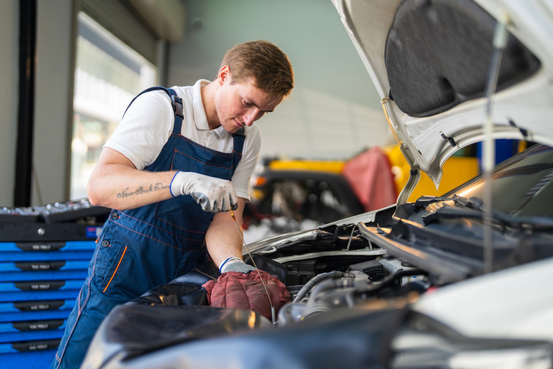 Mechanic working under the hood of a vehicle inside a professional auto repair shop.