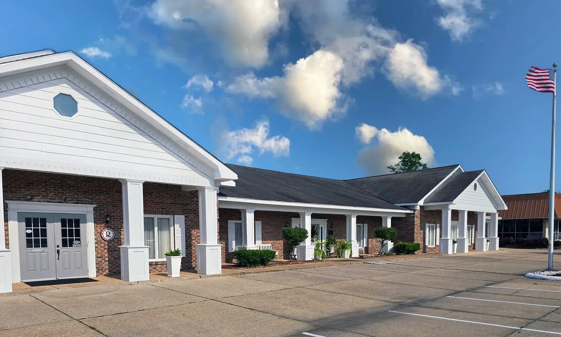White single-story building with columns, parking lot, and an American flag under a blue sky