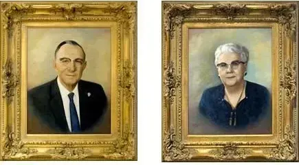 Two framed painted portraits of a man and a woman hanging side by side on a white wall.