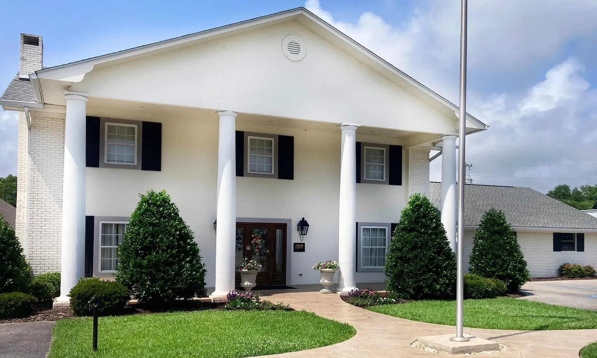 White two-story house with columns, black shutters, and a green lawn under a clear sky