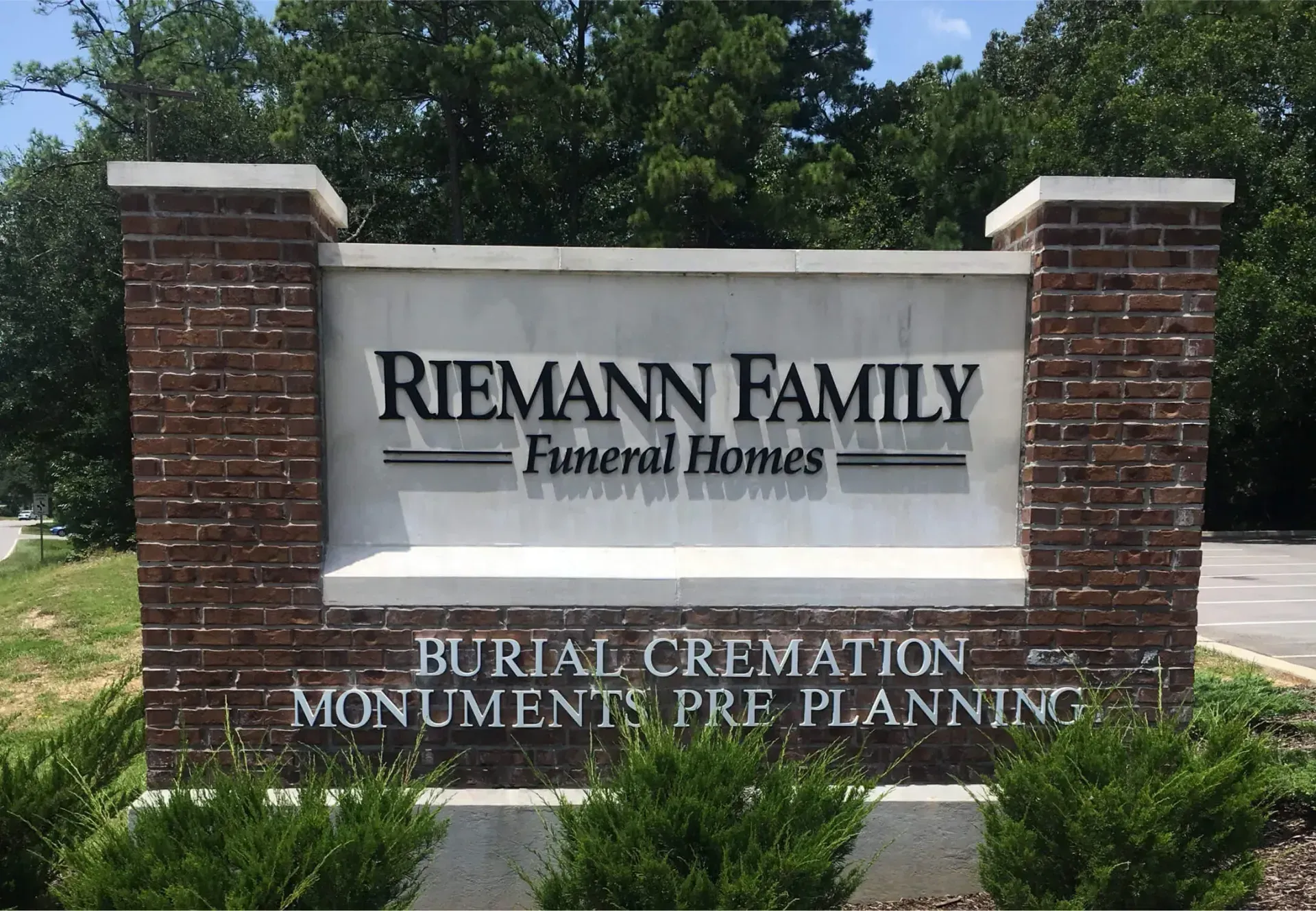 Riemann Family Funeral Homes sign on brick pillars with trees in the background