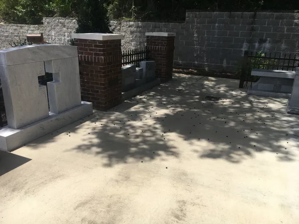 Sunny concrete patio with brick pillars, a stone wall, and dappled tree shadows.