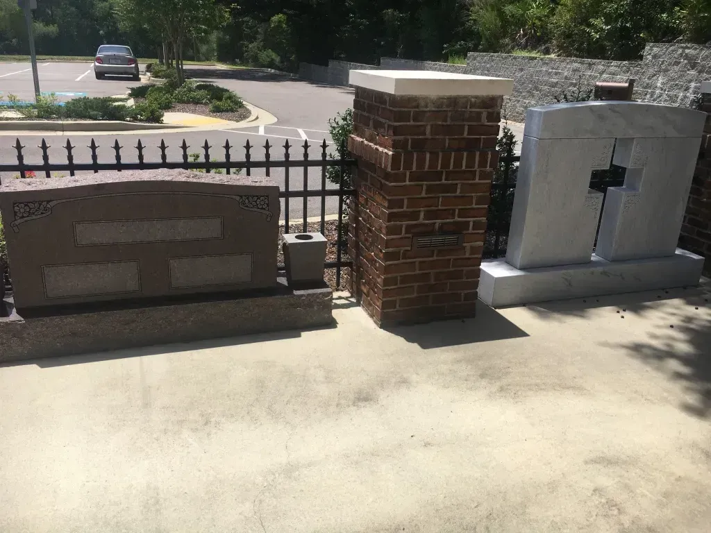 Brick and stone outdoor memorial wall beside a black metal fence and parking lot