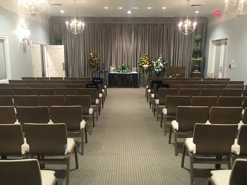 Empty ceremony room with rows of chairs facing a floral-decorated stage and gray curtains