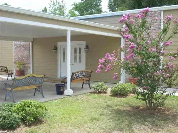 Covered patio with wicker chairs, white doors, and a blooming pink crepe myrtle in a landscaped yard