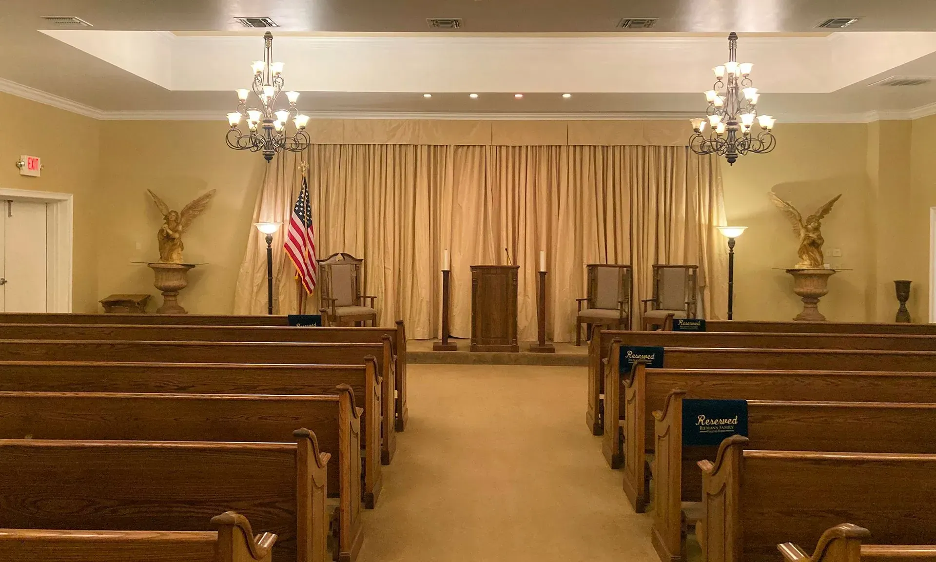 Empty courtroom with wooden benches, judges' bench, American flag, and chandeliers under warm lighting