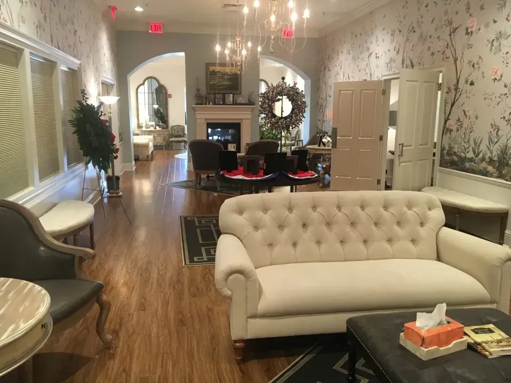 Elegant lounge with cream sofas, hardwood floors, floral wallpaper, and a fireplace at the far end
