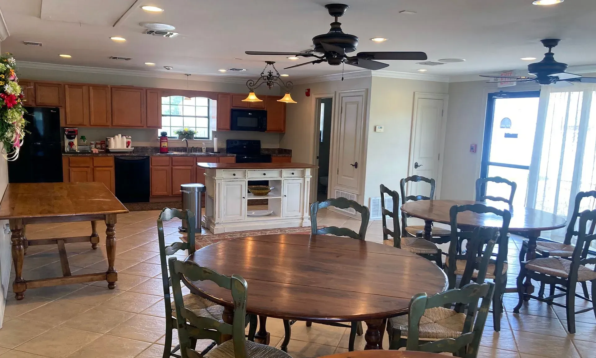 Spacious open-plan kitchen and dining area with wooden tables, chairs, ceiling fans, and sliding glass doors