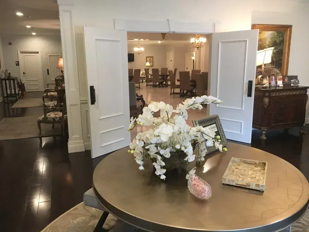 Flower arrangement on a round table in a bright dining room with open white double doors and set tables beyond