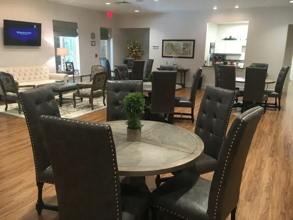 Lobby lounge with round tables, black chairs, and a wall-mounted TV on wood floors.