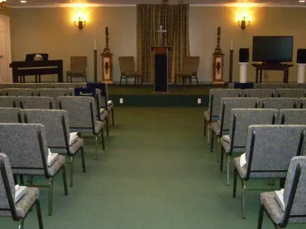 Empty church sanctuary with rows of gray chairs facing a raised altar and lectern under warm wall lights