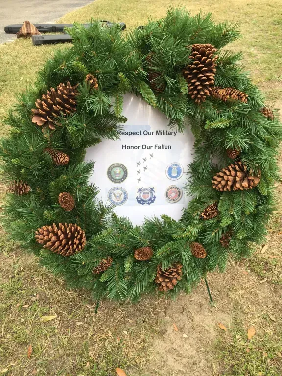 Pinecone memorial wreath on grass with a sign reading “Spirit Our Military, Honor Our Fallen.”