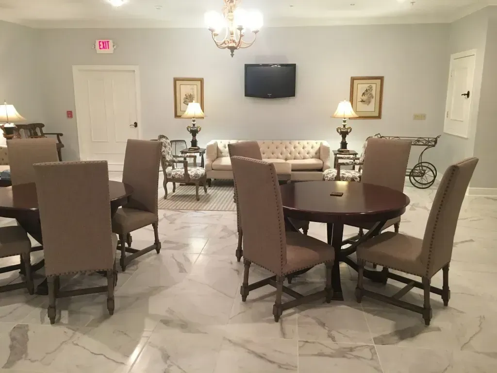 Elegant dining room with round tables, upholstered chairs, wall art, lamps, and a wall-mounted TV