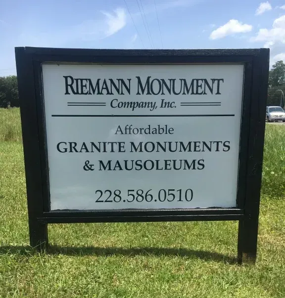 Sign for Riemann Monument Company advertising granite monuments and mausoleums, outdoors on grass