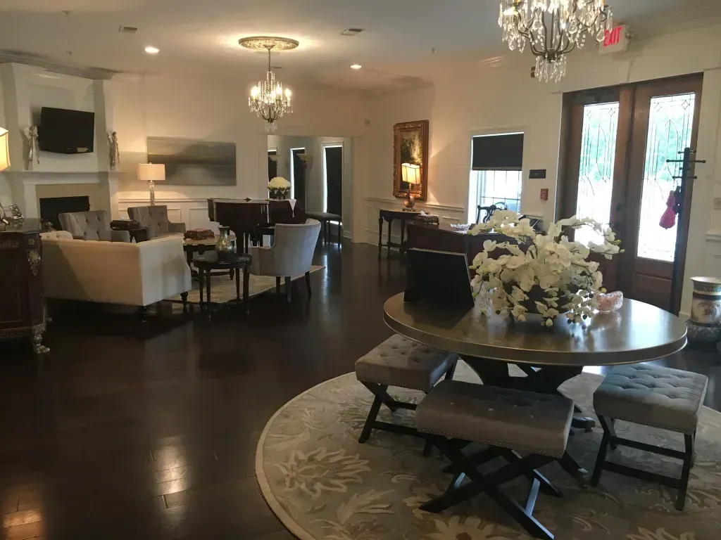 Elegant living room with dark wood floors, chandeliers, white sofas, and a round table with flowers.