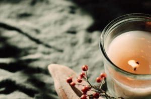 Candle in a glass jar with red berries and a small star ornament on a soft fabric background
